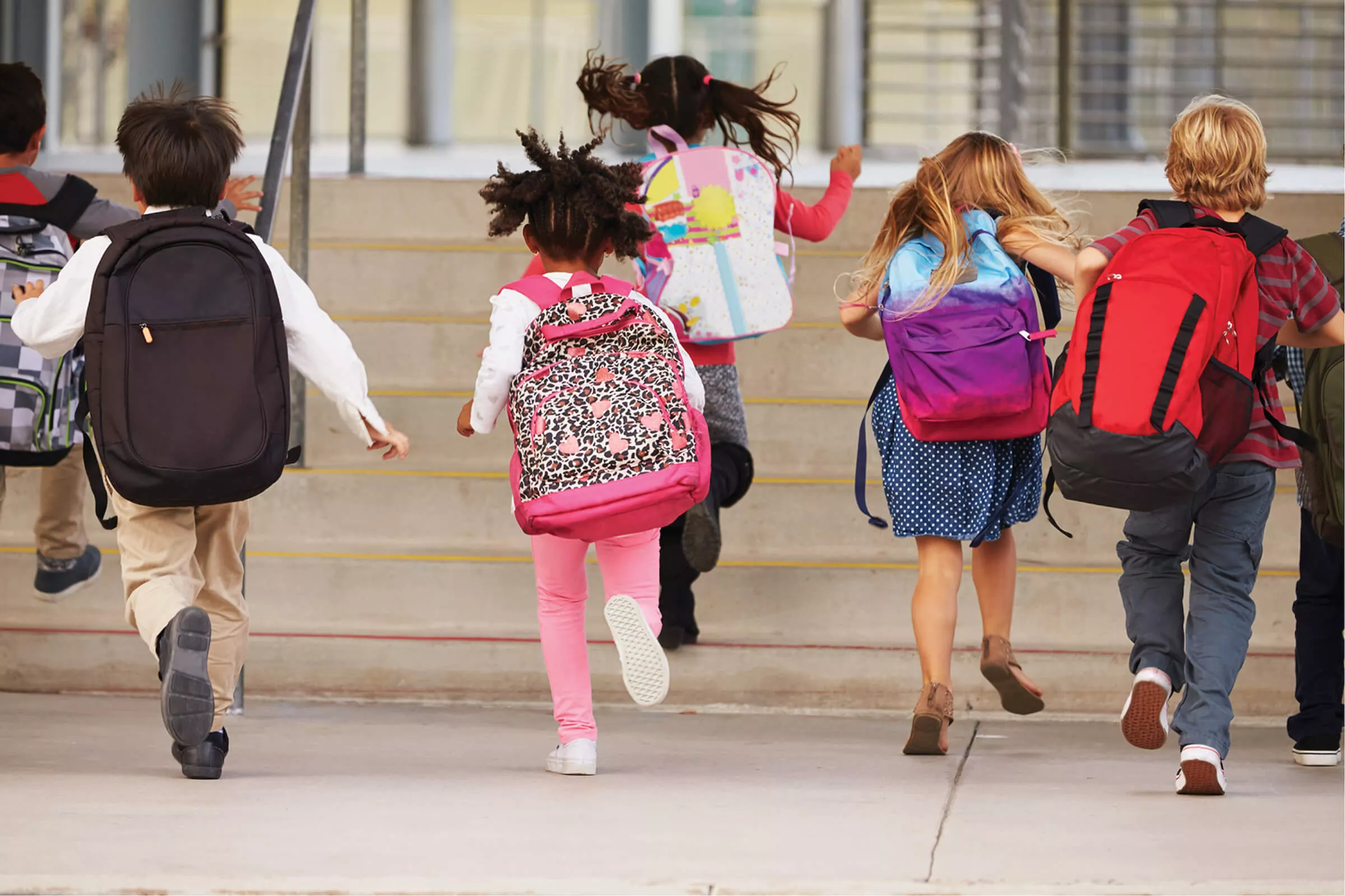 Several elementary children running up school stairs with backpacks on