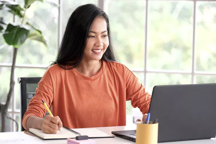 Person sitting at a desk taking notes from a laptop